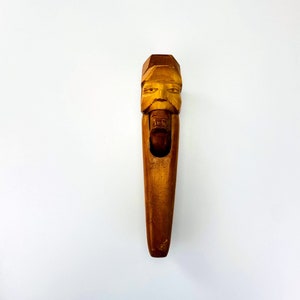 May include: A wooden nutcracker carved in the shape of a man's face. The nutcracker is brown and has a small hole in the mouth for cracking nuts.