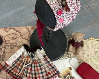 May include: A handmade doll wearing a red and white plaid dress with a red ribbon and a red and white crocheted hat with red buttons. The doll is sitting on a map with a red and white striped sock and a teddy bear.