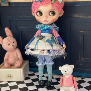 May include: A pink haired doll wearing a blue and white dress with a butterfly design. The doll is holding a small stuffed animal and is standing on a black and white checkered floor.