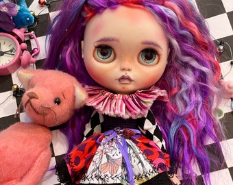 May include: A doll with long, curly, purple, pink, and blue hair, wearing a black and white checkered dress with a red, white, and floral print, and black and white striped stockings. The doll is sitting on a black and white checkered surface.