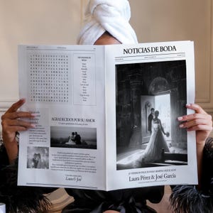 以下が含まれることがあります： 結婚をテーマにした内容の「NOTICIAS DE BODA」というタイトルの新聞を持っている人。新聞にはクロスワードパズル、結婚式の写真、そして「Laura Pérez & José García」という名前が掲載されています。その人は頭に白いタオルを巻いています。
