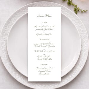 May include: A formal dinner setting with a white plate, gold silverware, and a menu card. The menu card lists the courses: Roasted Beet Salad, Lemon Roasted Chicken, and Chocolate Cherry Cake. Burgundy flowers and a lit candle add to the ambiance.