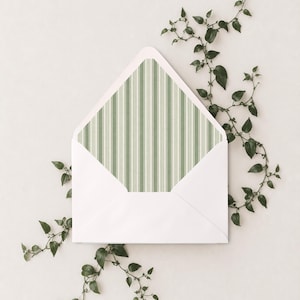 May include: A white envelope with an open flap revealing a sage green and white vertical striped liner. The envelope is surrounded by a delicate, thin vine with small green leaves that extends from the top right to the bottom left.