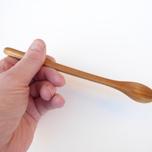 Könnte beinhalten: Ein langer, dünner Holzlöffel mit einer abgerundeten Schale. Der Löffel wird in einer Hand gehalten.