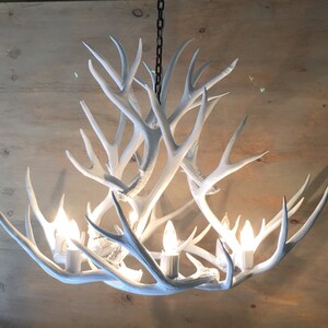 Puede incluir: Candelabro blanco de asta de ciervo con seis bombillas. Las astas est&aacute;n dispuestas en un patr&oacute;n circular y el candelabro cuelga de una cadena.