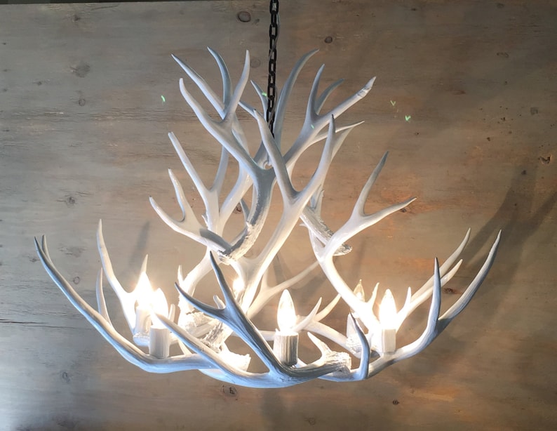 Puede incluir: Candelabro blanco de asta de ciervo con seis bombillas. Las astas est&aacute;n dispuestas en un patr&oacute;n circular y el candelabro cuelga de una cadena.