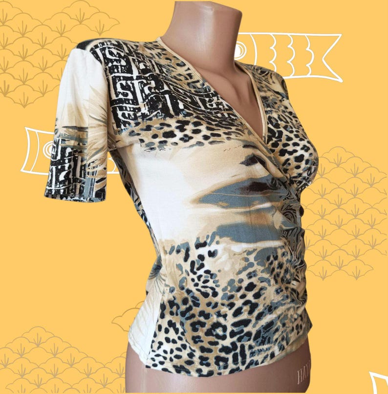 May include: A beige wrap-style top with short sleeves. The top features a mix of patterns, including leopard print, geometric shapes, and abstract designs in black, brown, and grey. The neckline is a V-shape.