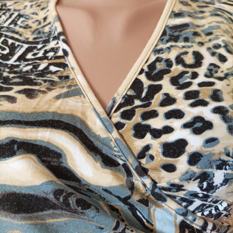 May include: A close-up of a wrap-style top with a V-neckline. The fabric features a mix of animal prints in shades of beige, black, and teal. The top is made of a soft, flowing material.