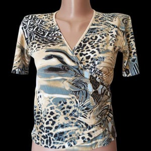 May include: A beige, blue, and black patterned wrap top with short sleeves. The top has a V-neck and a mix of animal print and abstract designs. The fabric appears lightweight, suitable for warmer weather.