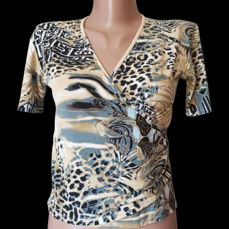 May include: A beige, blue, and black patterned wrap top with short sleeves. The top has a V-neck and a mix of animal print and abstract designs. The fabric appears lightweight, suitable for warmer weather.