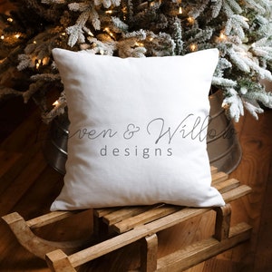 May include: A white pillow with the text "Loven & Willows designs" on a wooden sled in front of a snowy Christmas tree with lights.