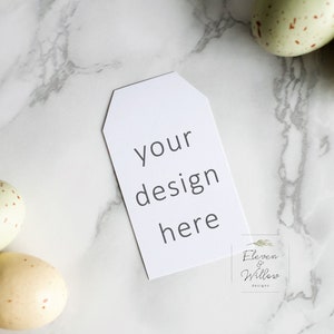 May include: A white gift tag with the text "your design here" on a marble background with speckled green and white Easter eggs.
