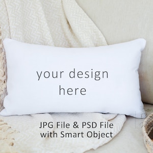 Puede incluir: Almohada blanca con el texto "your design here" en un sofá blanco con una manta blanca y una pequeña planta en maceta y una vela en el fondo. Archivo JPG y archivo PSD con objeto inteligente.