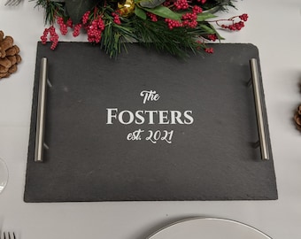Puede incluir: Una bandeja de servir de pizarra negra con asas plateadas. La bandeja tiene el texto "The Fosters est. 2021" grabado en blanco.