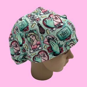 May include: A light teal surgical scrub cap featuring a repeating pattern of vintage illustrations. The design includes images of a woman, hands, tickets, and text. The cap is displayed on a mannequin head against a pink background.
