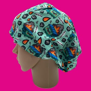 May include: A light teal surgical scrub cap with a repeating pattern of burning dumpsters, flames, smoke, and the phrase "THIS IS FINE." The cap is designed to cover the head and hair, commonly used in medical settings.
