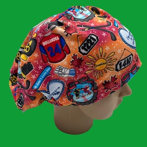Könnte beinhalten: Eine gemusterte OP-Haube mit Hockey-Motiven. Die Haube hat einen roten, orangefarbenen und gelben Hintergrund mit Hockeyschlägern, Handschuhen und dem Text "HOLLANDER 24". Weitere Texte sind "Sunshine" und Zahlen.