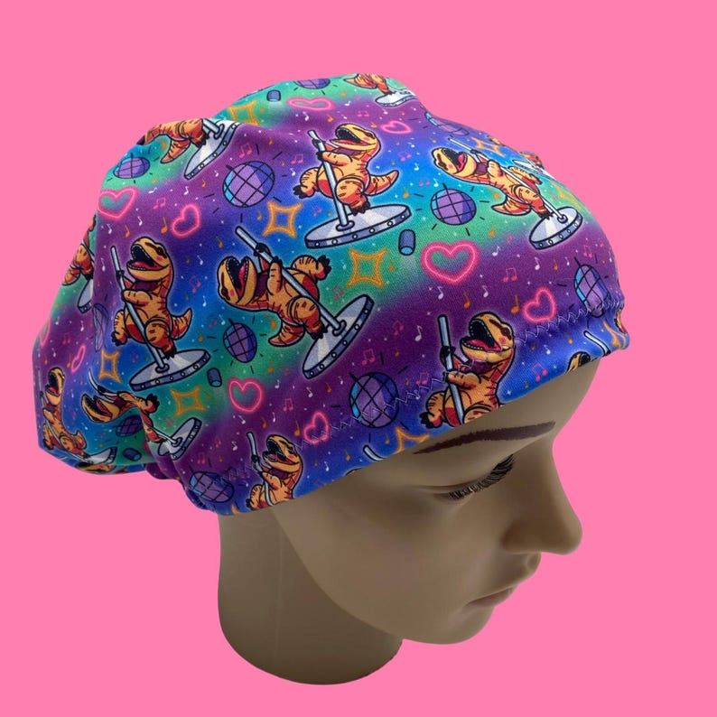 May include: A colorful scrub cap featuring a repeating pattern of orange cartoon dinosaurs pole dancing. The background is a vibrant mix of purple, blue, green, and yellow with hearts, disco balls, and musical notes.