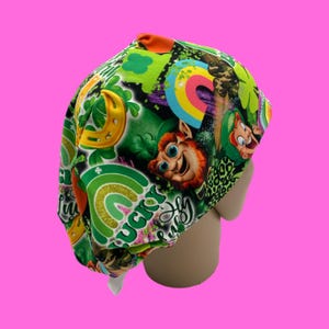 May include: Green, orange, and yellow patterned surgical scrub hat with a leprechaun and rainbows. The hat says "Lucky" on it.