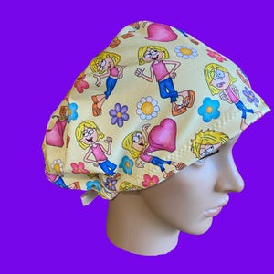 May include: A yellow scrub cap featuring a repeating cartoon print of a blonde character in a pink shirt and blue jeans, interspersed with colorful flowers and pink hearts. The fabric head covering has a gathered back and a contoured fit.