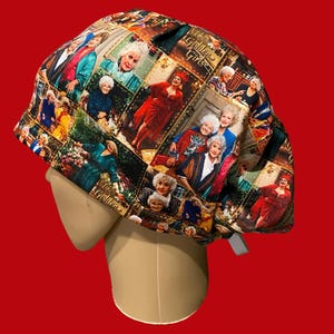 May include: A scrub cap featuring a colorful all-over print of scenes and characters from the television show The Golden Girls. The fabric displays multiple portraits of the four main characters in various outfits and settings with the show title text.