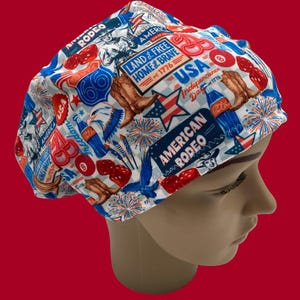 May include: A white, blue, and red patterned scrub cap featuring patriotic American symbols. The cap includes images of cowboy boots, fireworks, the American flag, and the text "American Rodeo" and "USA Independence Day".
