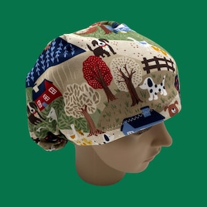 May include: A beige scrub cap with a whimsical farm scene print. The design features cartoon dogs, trees, houses, and a fence. The cap is made of fabric and is designed to cover the head.