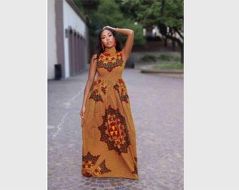 Op de afbeelding: Een vrouw draagt een lange, mouwloze jurk met een geometrische print in bruin, geel, rood en groen. De jurk heeft een hoge halslijn en een aansluitend bovenlijf.