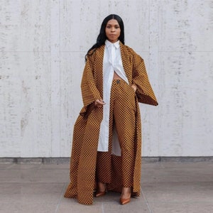 May include: A long brown and black patterned coat with a white collared shirt underneath. The coat has long sleeves and a wide, flowing silhouette.