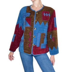 May include: A patchwork jacket in shades of blue, burgundy, and brown. The jacket features a round neckline, long sleeves, and gold-colored buttons. The design includes geometric shapes and embroidered details.