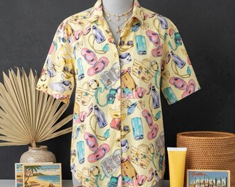 May include: A short-sleeve button-down shirt in a pale yellow hue featuring an all-over print of beach-themed illustrations including straw bags, flip-flops, sunscreen bottles, and sunglasses. The shirt has a classic collar and front buttons.