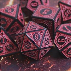 May include: A set of polyhedral dice featuring a deep red and black colour scheme. Each die has intricate, raised scrollwork patterns surrounding the black circular insets that contain clear, bold black numbers for easy reading during gameplay.
