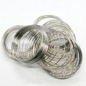 May include: A collection of silver-colored bangles. The bangles are thin, circular, and appear to be made of metal. They are stacked together, creating a layered effect. The bangles are displayed against a white background.