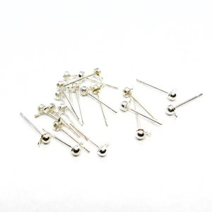 May include: A close-up of a pile of silver earring posts with a ball at the end. The posts are scattered on a white surface.