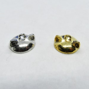 May include: Two metal pig-shaped charms. One charm is silver-colored, and the other is gold-colored. Each charm has a loop for attaching to a necklace or bracelet. The charms are small and detailed.