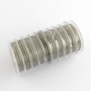 May include: A roll of silver-colored wire wrapped in clear plastic packaging. The wire is wound around a spool and there are multiple spools stacked together.