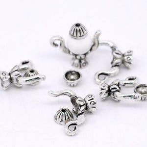 May include: Silver tone teapot charm with a white pearl-like center. The charm is made up of several pieces, including a teapot, a lid, a handle, and a spout. The charm is perfect for adding a touch of whimsy to jewelry or crafts.