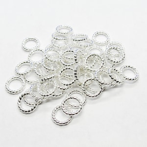 May include: A pile of silver jump rings, each with a twisted or rope-like design. The rings are small and perfect for jewelry making.