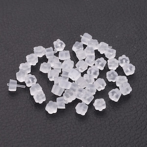 May include: A pile of clear plastic earring backs. The backs are shaped like a flower with a small post on the bottom.