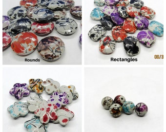 May include: Assortment of colorful painted ceramic beads in round, rectangular, and flower shapes. The beads have a white base with black, red, blue, and purple paint splatters.