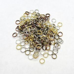 May include: A large pile of mixed metal jump rings in silver, gold, and bronze colors. The jump rings are all different sizes and are perfect for jewelry making.
