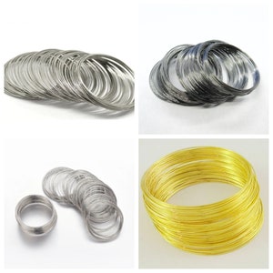 May include: A set of three different colored wire rings. The rings are silver, black, and gold. The rings are stacked on top of each other.