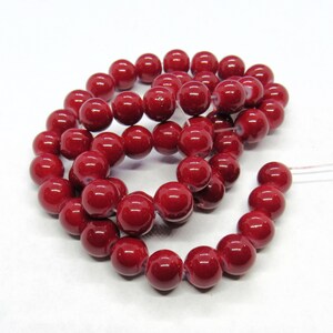 May include: A strand of deep red glass beads. The beads are round and have a glossy finish.