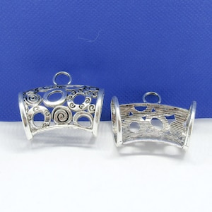 May include: Two silver metal pendant caps with decorative designs. One cap has a swirl pattern and the other has a star pattern.