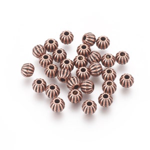May include: A pile of copper-colored metal beads with a ribbed design. The beads are round and have a hole in the center for stringing.