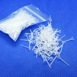 May include: A clear plastic bag filled with a large quantity of small, clear plastic flower stem tips. The tips are scattered on a blue surface.