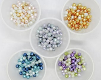 May include: Five small white bowls each filled with a different color of pearl beads. The colors are white, light blue, lavender, green, and gold.