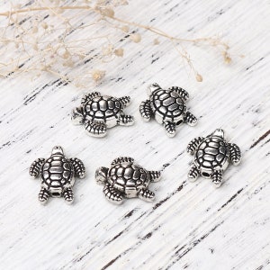 May include: Five silver turtle charms featuring intricate shell designs. The charms are small and ideal for adding a touch of whimsy to jewellery or crafts.