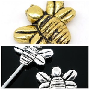 May include: Two bee-shaped metal charms, one gold and one silver. Both charms have a striped pattern on their bodies and wings.