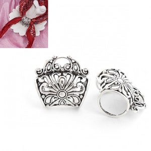 May include: Two silver-colored scarf rings with an ornate floral design. One ring is upright, showcasing the front, while the other is on its side, revealing the hollow interior. The rings have a vintage, antique aesthetic.